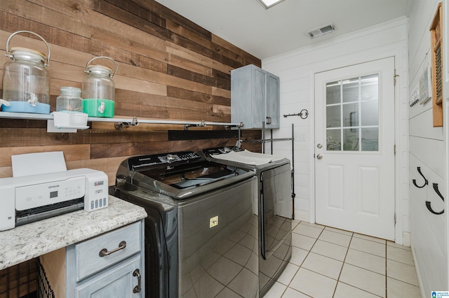 laundry room featuring washer and dryer, light tile patterned floors, cabinets, and wooden walls