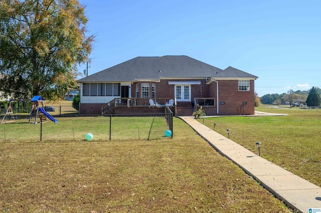 back of house with a lawn, a sunroom, and a playground