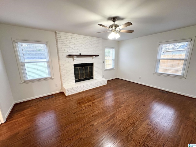 unfurnished living room with a healthy amount of sunlight, ceiling fan, a fireplace, and dark wood-type flooring