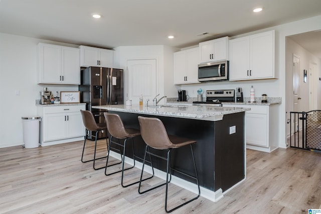 kitchen featuring white cabinets, light wood-type flooring, stainless steel appliances, and an island with sink