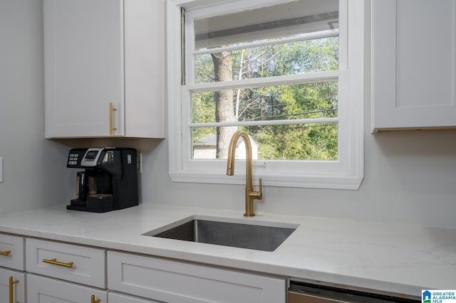 kitchen featuring white cabinets, stainless steel dishwasher, light stone countertops, and sink