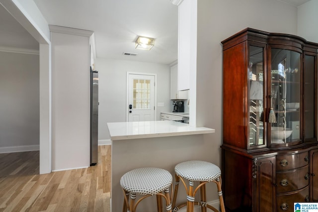 kitchen featuring kitchen peninsula, light wood-type flooring, a breakfast bar, white cabinets, and ornamental molding