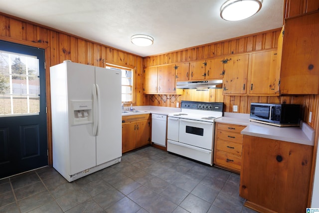 kitchen with white appliances, wooden walls, and sink