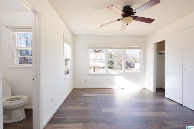 unfurnished bedroom with multiple windows, dark hardwood / wood-style flooring, ensuite bathroom, and ceiling fan