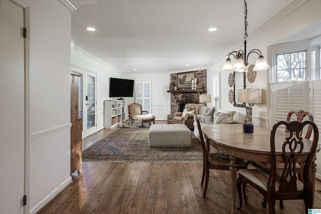 dining area featuring dark wood-type flooring, french doors, crown molding, a fireplace, and a notable chandelier