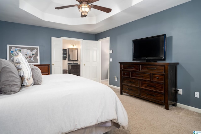 carpeted bedroom featuring a tray ceiling, ensuite bath, and ceiling fan