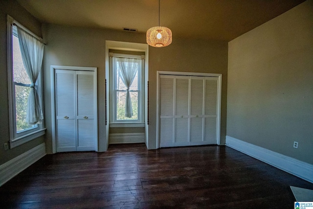 unfurnished bedroom featuring multiple windows, dark hardwood / wood-style flooring, and two closets