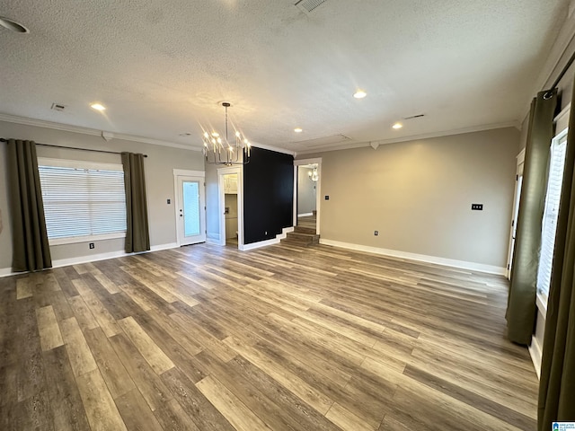 unfurnished living room featuring a healthy amount of sunlight, hardwood / wood-style flooring, an inviting chandelier, and crown molding