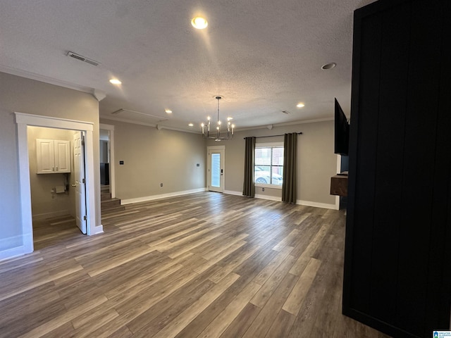 unfurnished living room with a textured ceiling, wood-type flooring, a notable chandelier, and ornamental molding