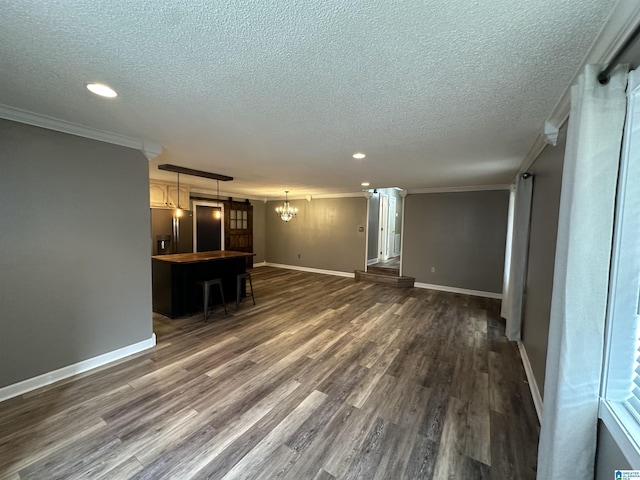 unfurnished living room with a textured ceiling, a notable chandelier, crown molding, and dark wood-type flooring