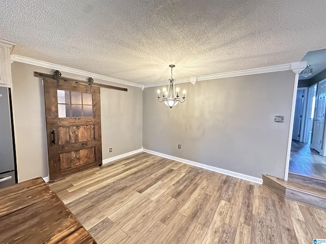 unfurnished room featuring a barn door, ornamental molding, a textured ceiling, and an inviting chandelier