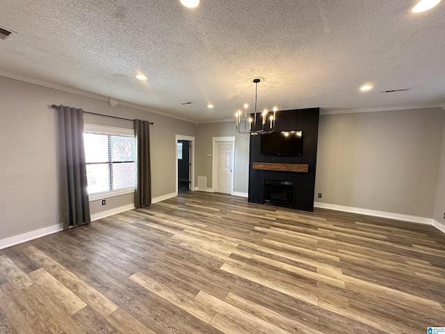 unfurnished living room with a large fireplace, an inviting chandelier, ornamental molding, a textured ceiling, and hardwood / wood-style flooring