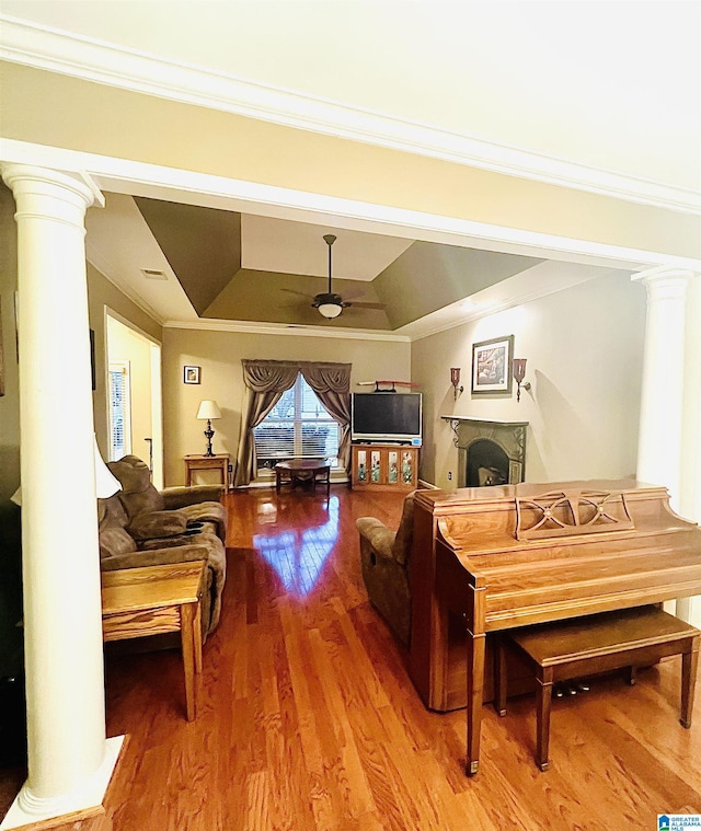 living room featuring wood-type flooring, a raised ceiling, ceiling fan, and ornamental molding