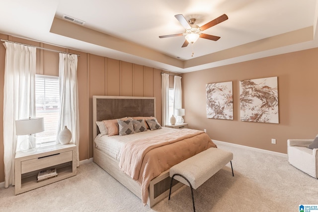 carpeted bedroom with a raised ceiling and ceiling fan