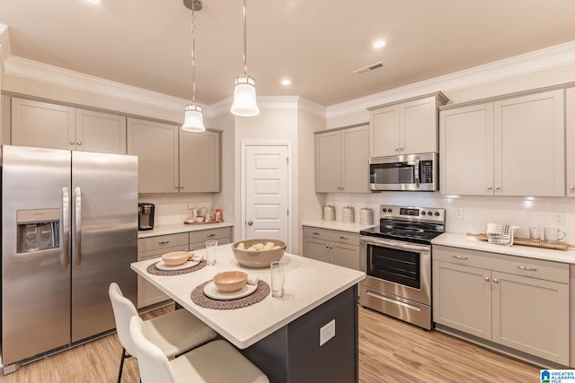 kitchen with a kitchen bar, appliances with stainless steel finishes, light hardwood / wood-style floors, a kitchen island, and hanging light fixtures