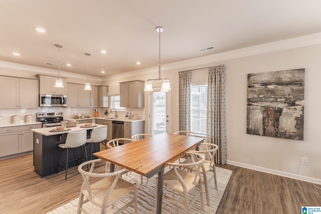 dining space with light hardwood / wood-style floors, plenty of natural light, crown molding, and sink