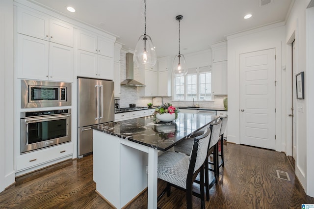 kitchen with a center island, stainless steel appliances, wall chimney range hood, a kitchen breakfast bar, and white cabinets