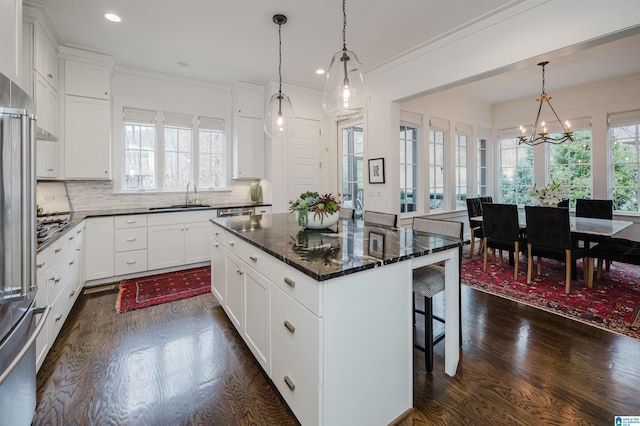 kitchen with white cabinetry, sink, decorative light fixtures, a breakfast bar area, and a kitchen island