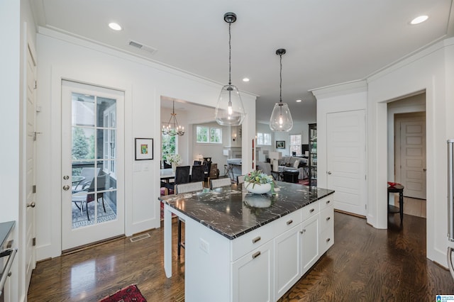 kitchen with a center island, hanging light fixtures, dark stone countertops, a breakfast bar, and white cabinets