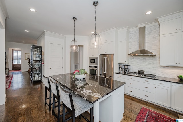 kitchen featuring white cabinetry, a kitchen island, stainless steel appliances, and wall chimney range hood