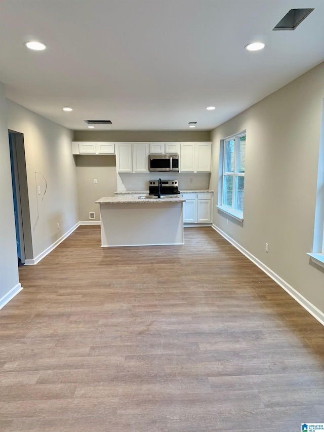 kitchen with light stone counters, white cabinets, stainless steel appliances, and light wood-type flooring