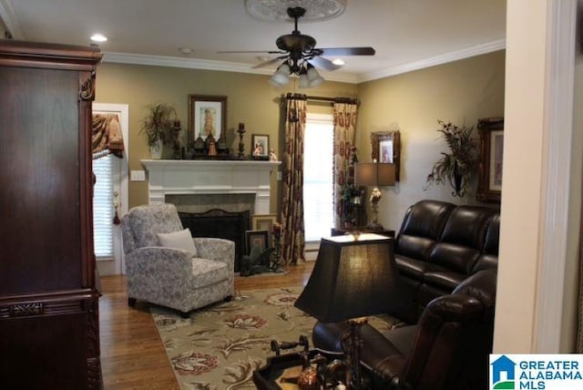 living area with a premium fireplace, crown molding, ceiling fan, and wood-type flooring