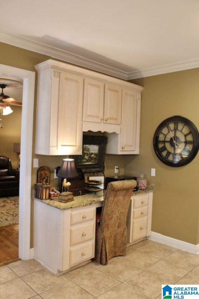 kitchen featuring crown molding, ceiling fan, built in desk, light tile patterned flooring, and light stone counters