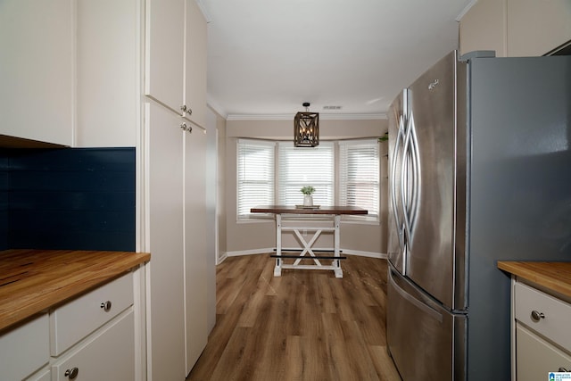 kitchen featuring crown molding, stainless steel fridge, butcher block countertops, decorative light fixtures, and white cabinetry