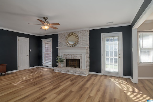 unfurnished living room featuring ceiling fan, light wood-type flooring, ornamental molding, and a brick fireplace