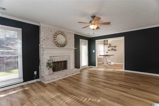 unfurnished living room featuring ceiling fan, a healthy amount of sunlight, ornamental molding, and a brick fireplace