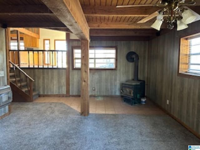 unfurnished living room featuring a wood stove, ceiling fan, beamed ceiling, plenty of natural light, and wood ceiling