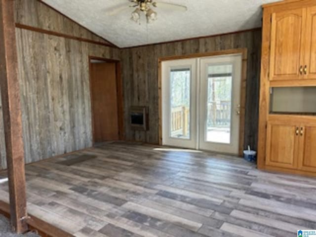 unfurnished living room with ceiling fan, french doors, heating unit, vaulted ceiling, and wooden walls