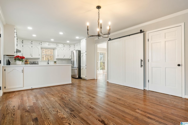 kitchen with stainless steel fridge, tasteful backsplash, a barn door, hardwood / wood-style flooring, and white cabinets