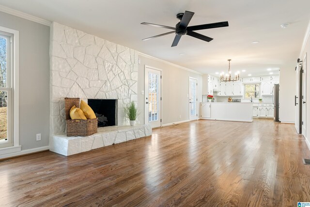 unfurnished living room with ceiling fan with notable chandelier, wood-type flooring, a fireplace, and ornamental molding