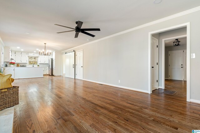 unfurnished living room with a barn door, crown molding, ceiling fan with notable chandelier, and dark hardwood / wood-style floors