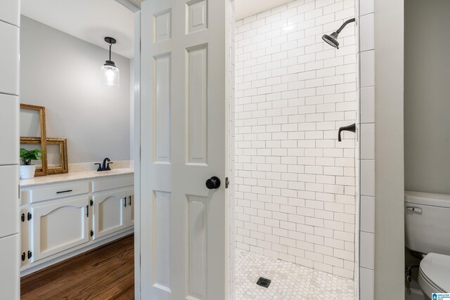 bathroom with hardwood / wood-style floors, toilet, a tile shower, and vanity