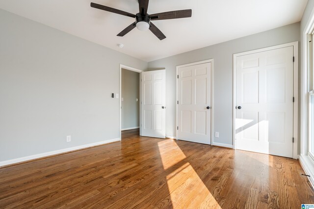 unfurnished bedroom featuring ceiling fan, wood-type flooring, and multiple closets