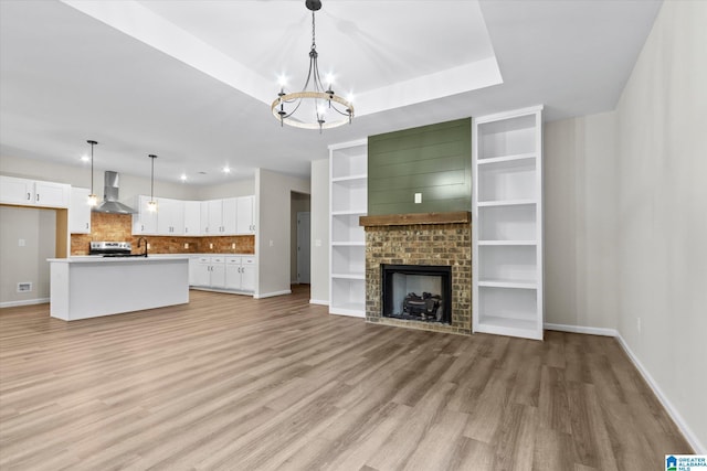 unfurnished living room with a raised ceiling, sink, light hardwood / wood-style flooring, an inviting chandelier, and a fireplace