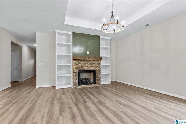 unfurnished living room with a notable chandelier, light hardwood / wood-style floors, a raised ceiling, and a brick fireplace