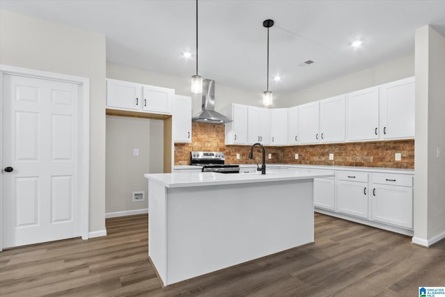 kitchen featuring stainless steel electric range oven, white cabinets, an island with sink, and wall chimney range hood