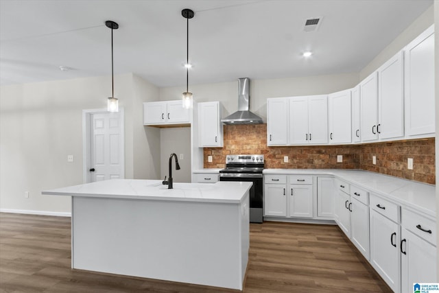 kitchen featuring stainless steel electric stove, wall chimney range hood, decorative light fixtures, white cabinets, and an island with sink