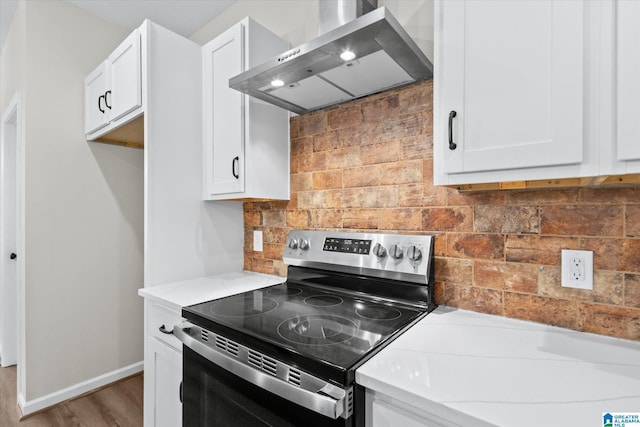 kitchen featuring white cabinetry, wall chimney exhaust hood, light stone counters, backsplash, and electric stove