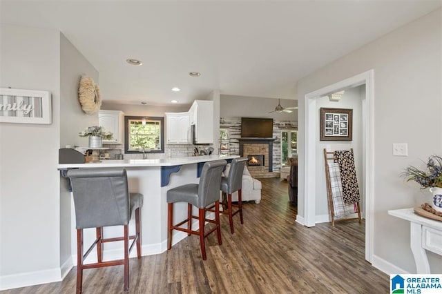 kitchen with kitchen peninsula, a kitchen breakfast bar, decorative backsplash, dark wood-type flooring, and white cabinetry