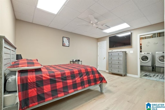 bedroom featuring washer and clothes dryer, ceiling fan, light hardwood / wood-style floors, and a drop ceiling