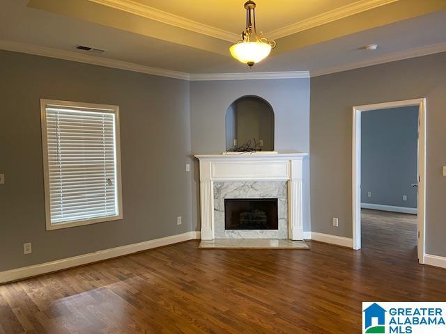 unfurnished living room featuring a tray ceiling, a high end fireplace, dark hardwood / wood-style floors, and ornamental molding