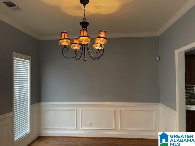 unfurnished dining area featuring hardwood / wood-style floors, ornamental molding, and a chandelier