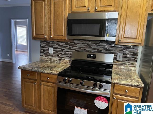 kitchen with backsplash, light stone countertops, dark wood-type flooring, and appliances with stainless steel finishes