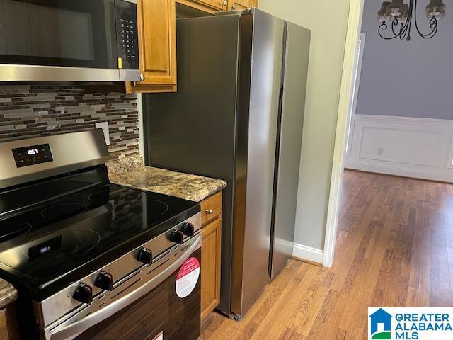 kitchen with light stone countertops, tasteful backsplash, a notable chandelier, appliances with stainless steel finishes, and light wood-type flooring