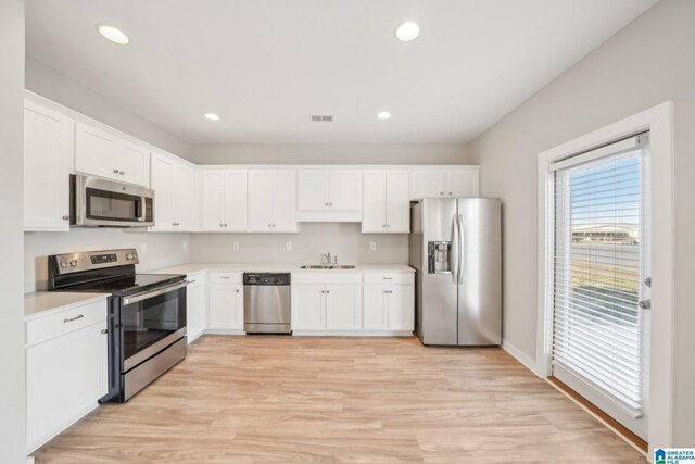 kitchen with appliances with stainless steel finishes, light hardwood / wood-style flooring, white cabinetry, and sink