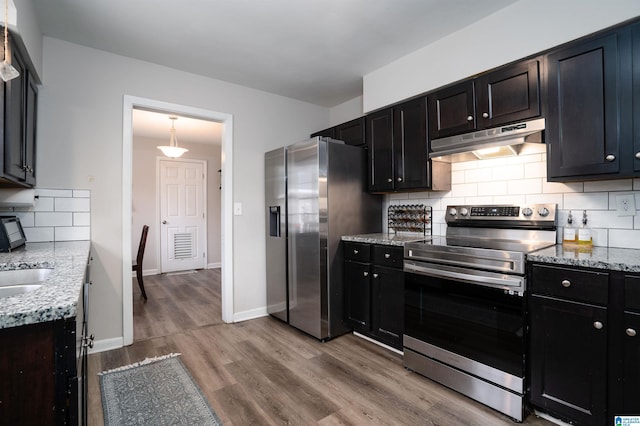 kitchen with light stone countertops, light hardwood / wood-style flooring, appliances with stainless steel finishes, and tasteful backsplash